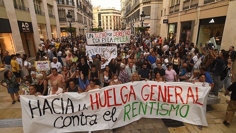 Manifestación ciudadana por el derecho a la vivienda recorriendo una calle peatonal flanqueada por edificios y tiendas, con personas sosteniendo pancartas reivindicativas.