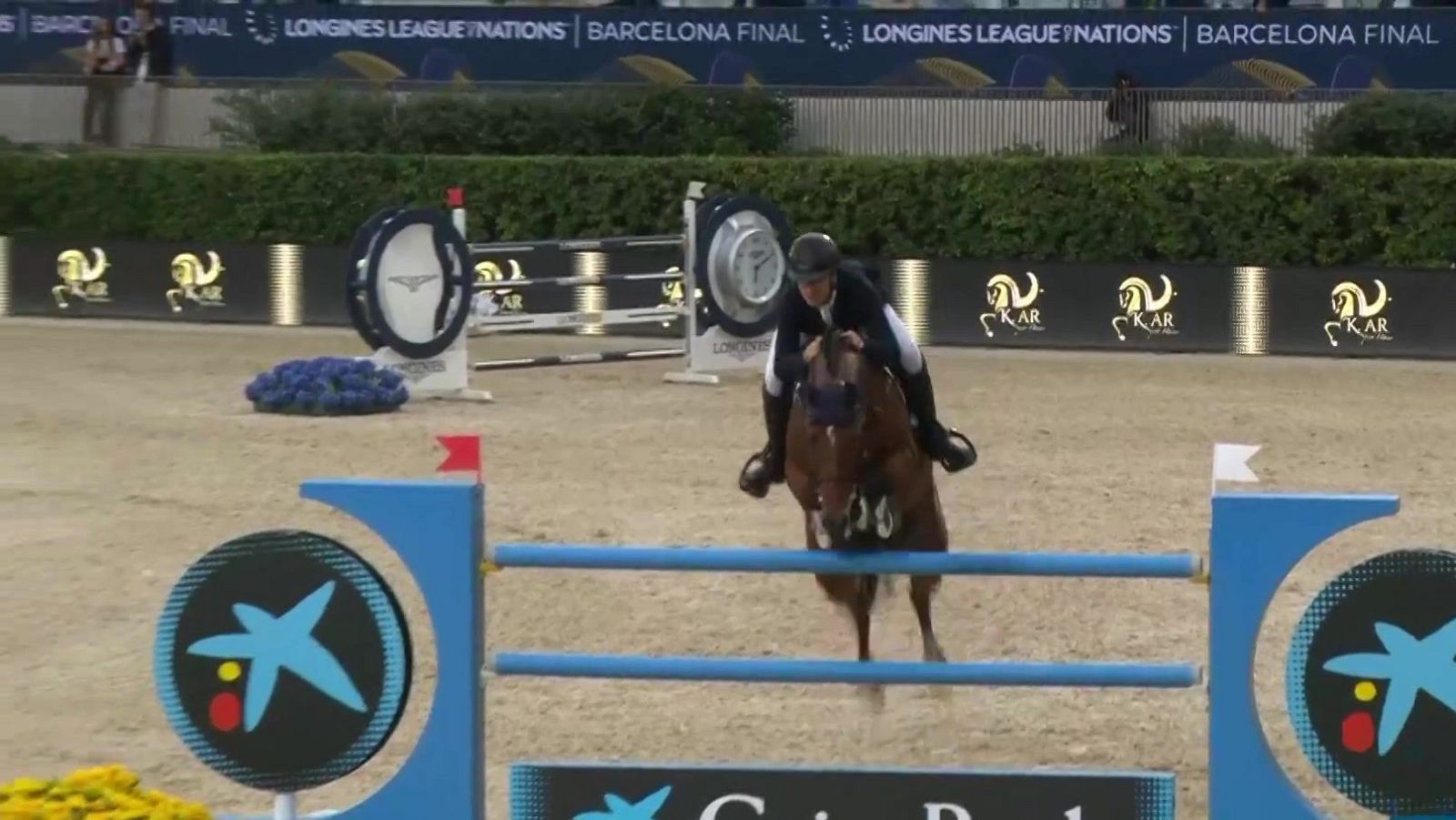 Jinete y caballo saltando un obstáculo en una competición hípica con elementos de CaixaBank y Longines.