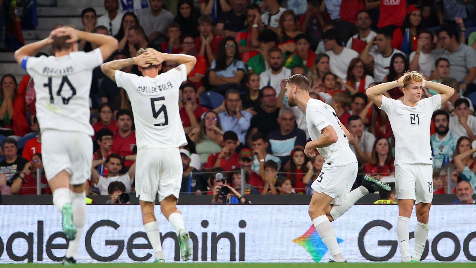 Futbolistas de la selección de Noruega celebran un gol sobre el terreno de juego durante un encuentro oficial con vallas publicitarias de Google Gemini y público al fondo.