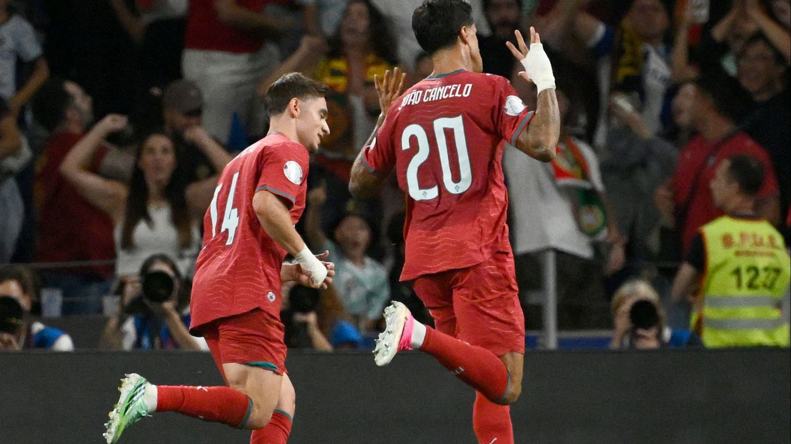 El jugador João Cancelo celebra un gol vistiendo la equipación roja de Portugal con el dorsal 20, en un estadio nocturno lleno de aficionados.