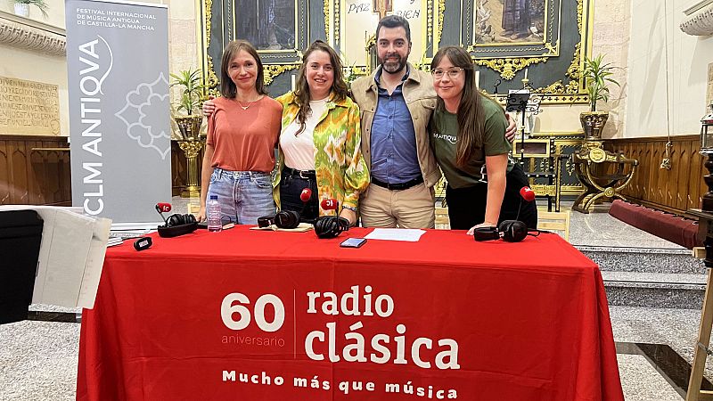 Cuatro personas posan sonrientes tras una mesa de radio en un edificio histórico con micrófonos, auriculares y un cartel de festival.