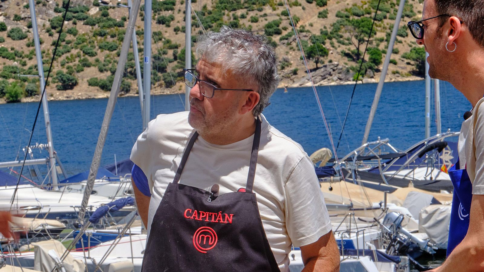 Florentino Fernández con delantal de capitán y delantal azul de otro concursante en un puerto deportivo con veleros.