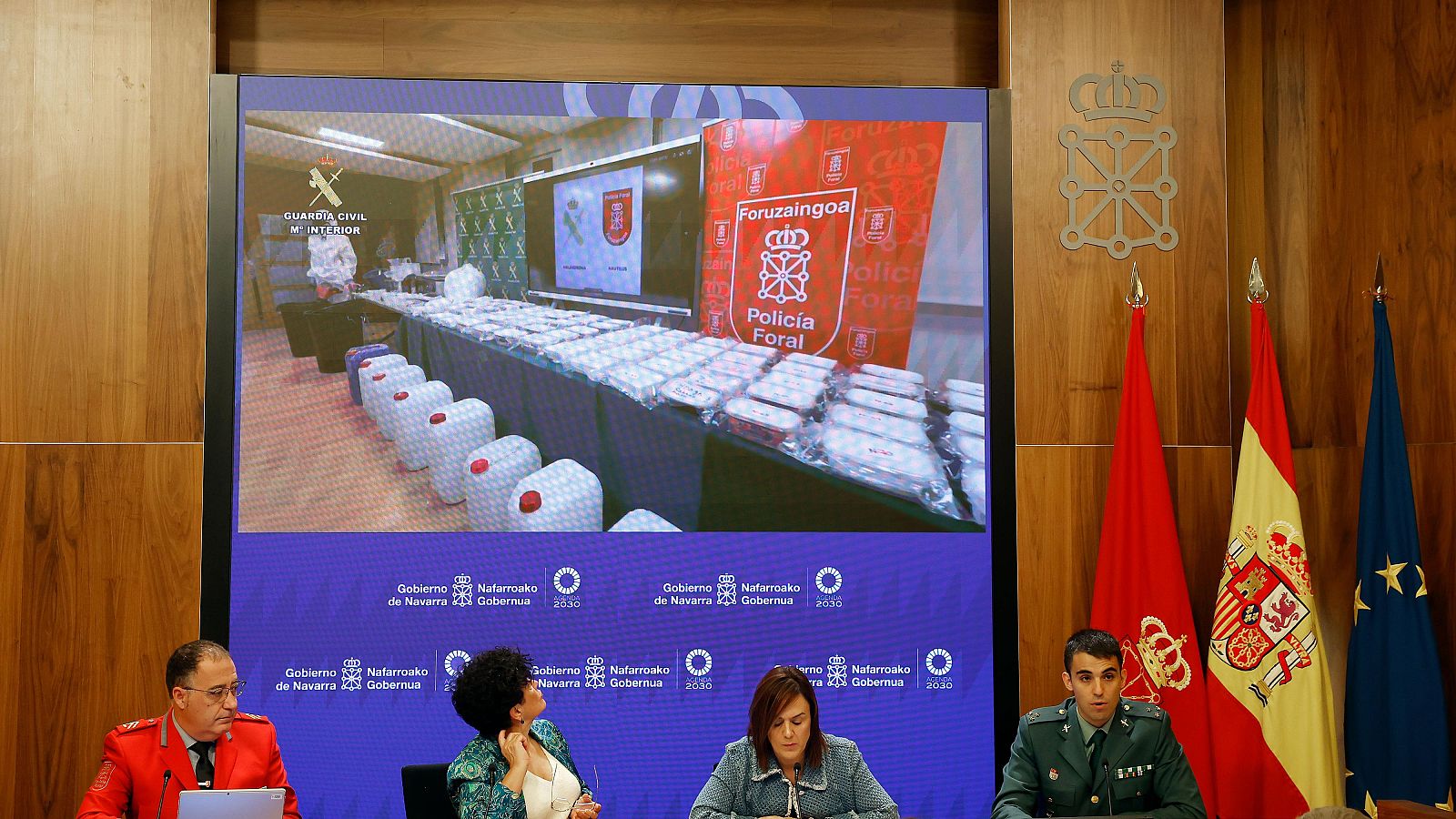 Cuatro ponentes en una sala de prensa ante una pantalla con imágenes de droga incautada y banderas institucionales.