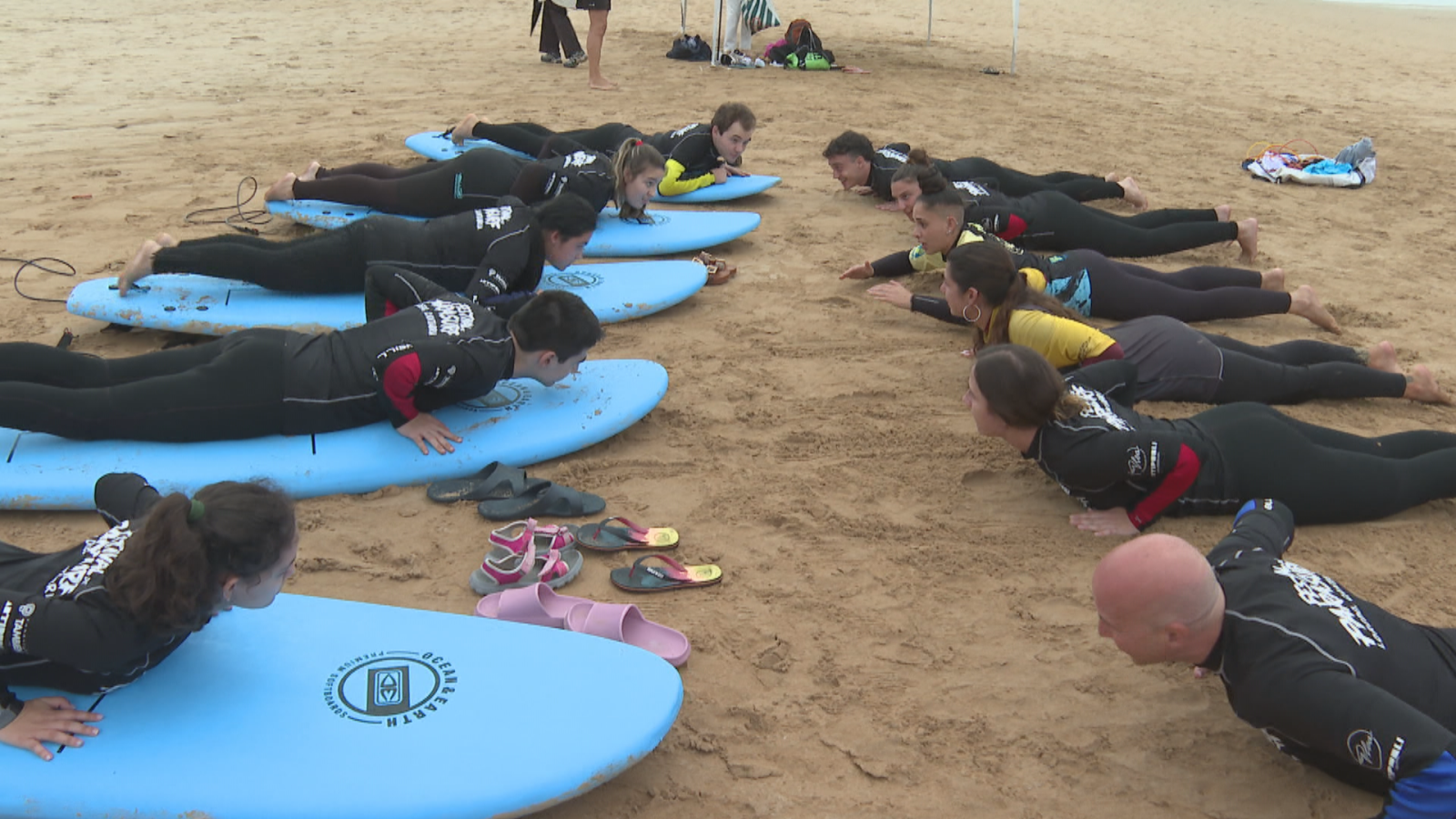 Participantes con neopreno practican la técnica de remada en la arena junto a tablas de surf.