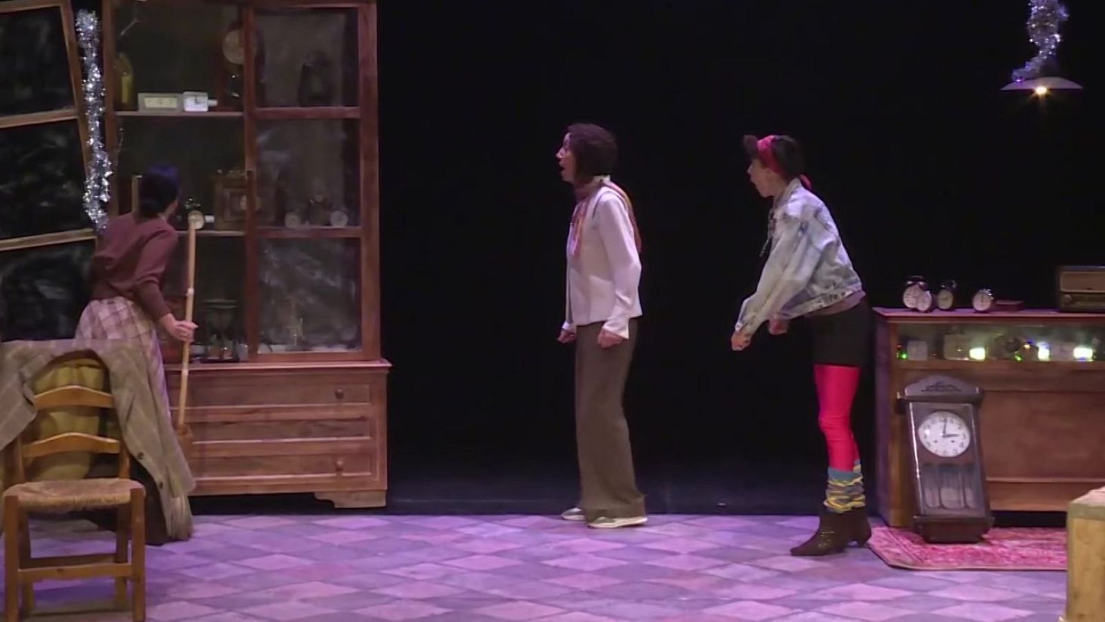 Tres actrices actúan en un escenario con atrezo clásico y detalles navideños, incluyendo una mujer con ropa ochentera y mallas rosas a la derecha.