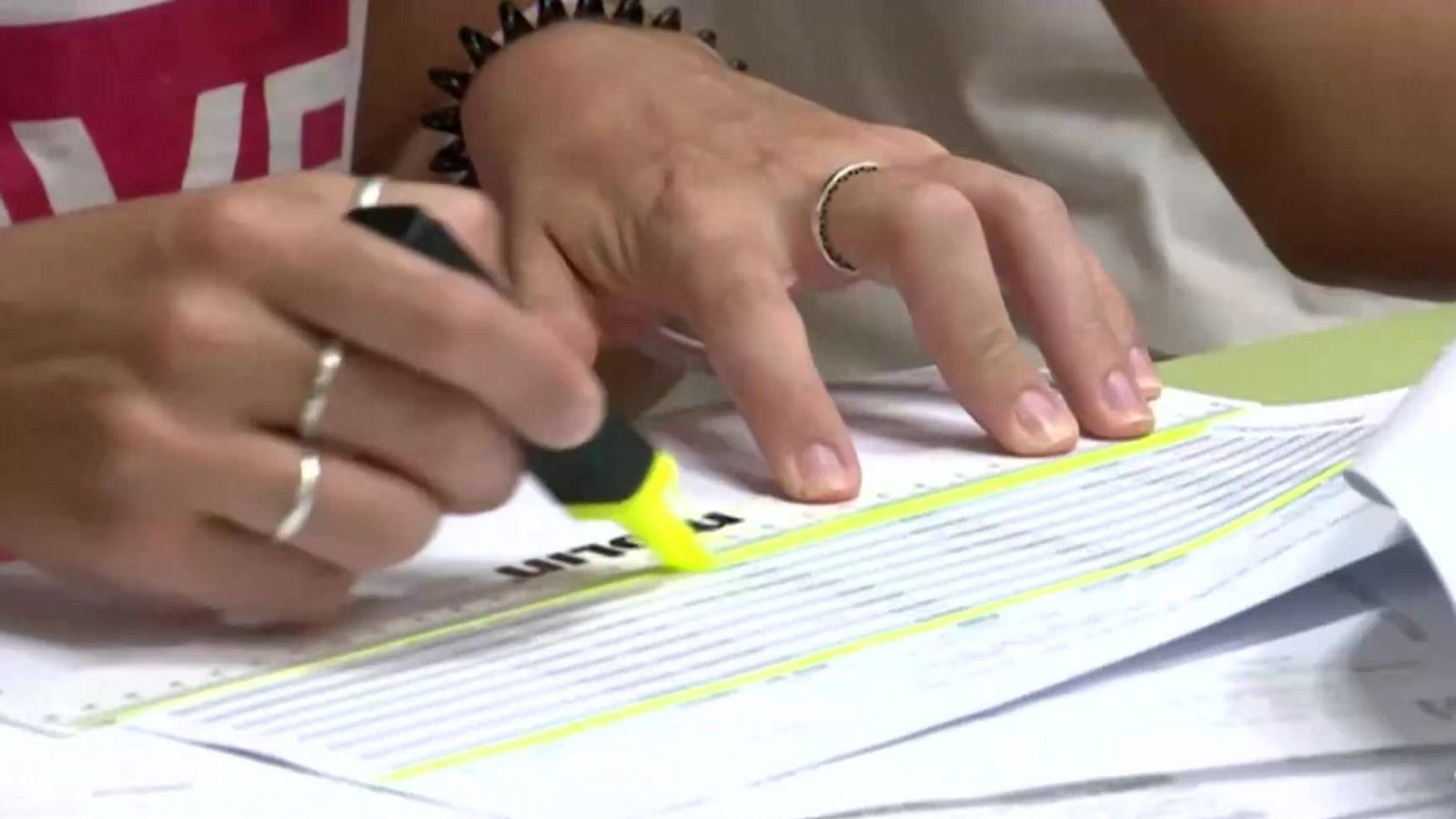 Primer plano de manos subrayando un documento impreso con rotulador amarillo fluorescente en una mesa de oficina.
