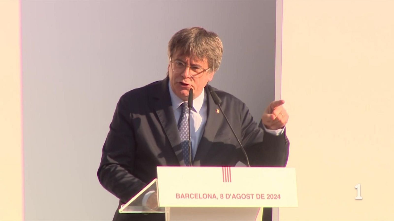 Plano medio de Carles Puigdemont gesticulando y señalando con el dedo detrás de un atril con el logotipo de la bandera catalana.