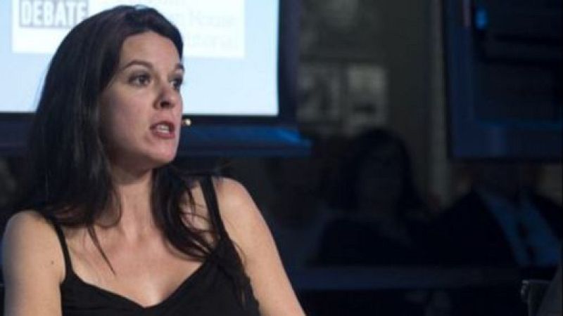 Plano medio de la política Inés Arrimadas hablando en un acto público con un top negro y micrófono de diadema, ante un fondo desenfocado.