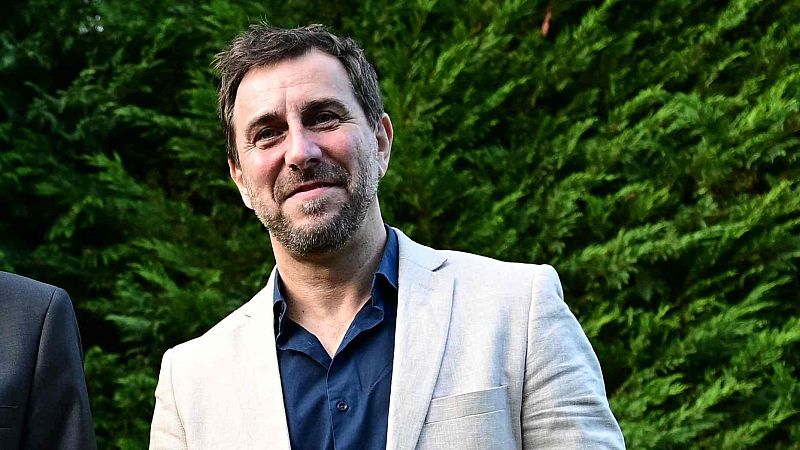 Primer plano medio del periodista Pablo González mirando al frente con sonrisa serena, vistiendo chaqueta beige y camisa azul.