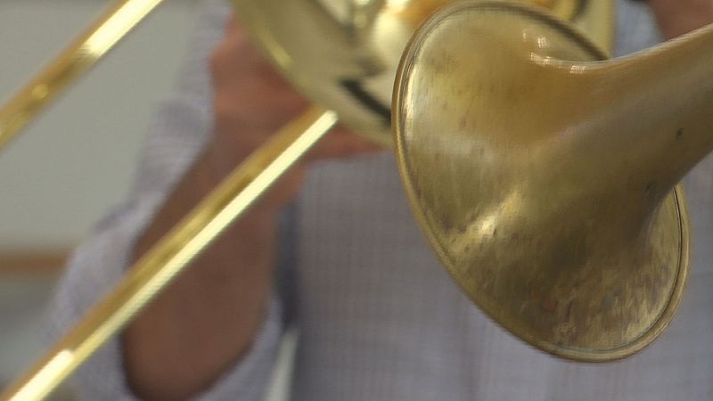 Plano de detalle de un trombón de varas dorado brillante durante una interpretación musical en un interior.