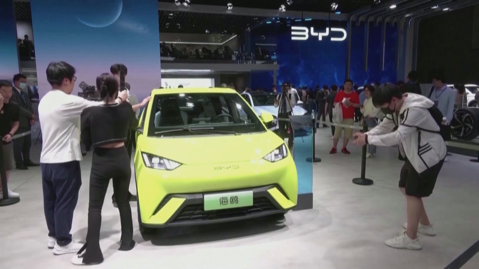 Stand de BYD en una feria del motor con un coche eléctrico verde lima siendo fotografiado por los asistentes.
