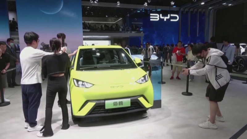 Stand de BYD en una feria del motor con un coche eléctrico verde lima siendo fotografiado por los asistentes.