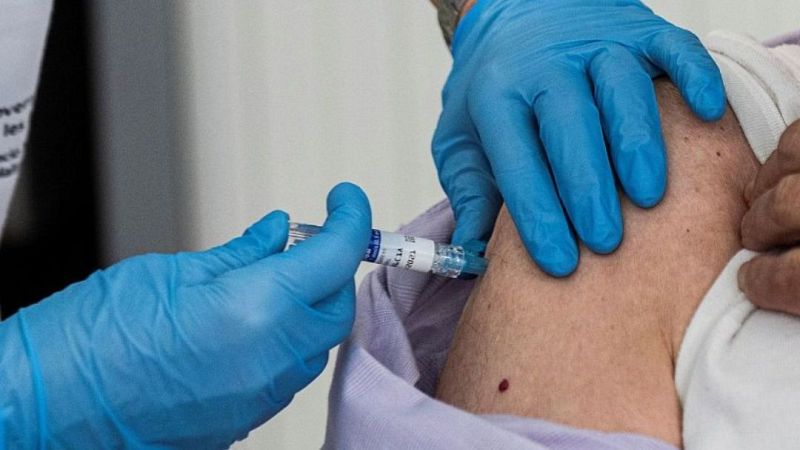 Un sanitario con guantes azules y uniforme blanco administra una inyección en el brazo de un paciente.