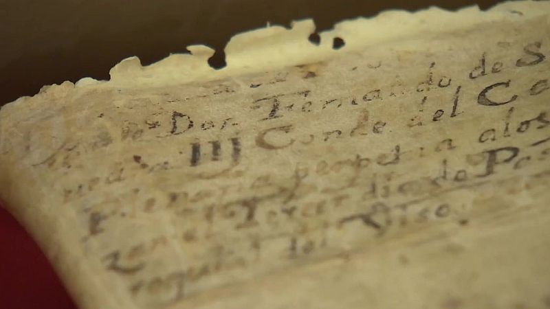 Plano de detalle de un manuscrito histórico en pergamino envejecido con trazos de tinta sepia y bordes rasgados.