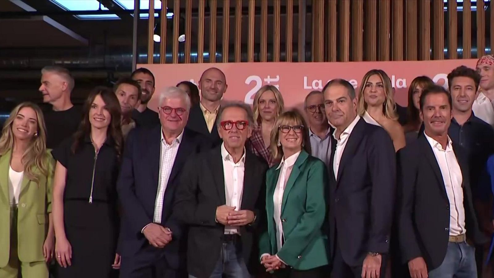 Un grupo de profesionales de la televisión posa sonriente frente a un panel promocional con Jordi Hurtado y Gemma Nierga en el centro.