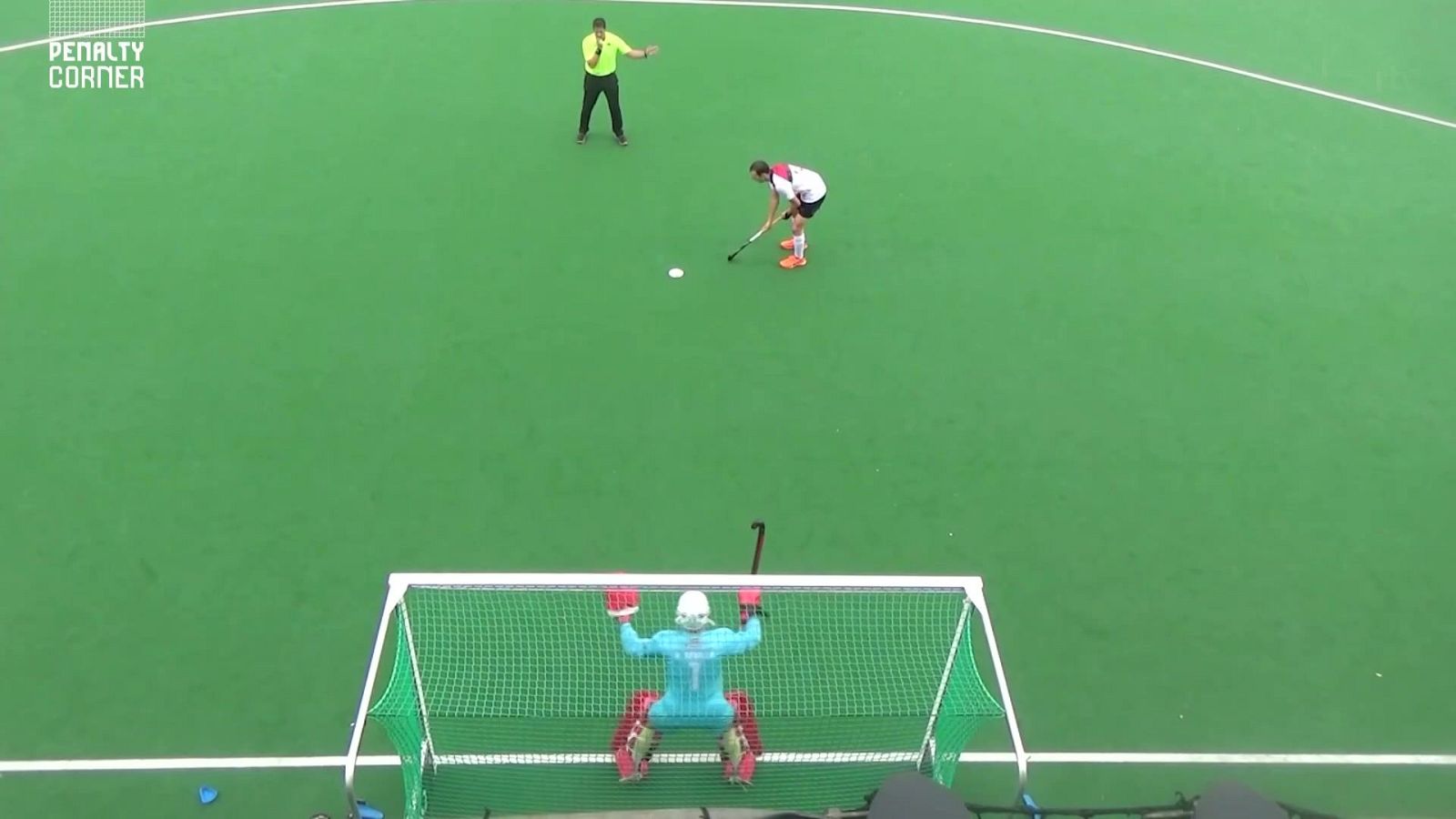 Vista cenital de un penalti de hockey sobre hierba con el lanzador frente al portero y el árbitro supervisando la jugada.