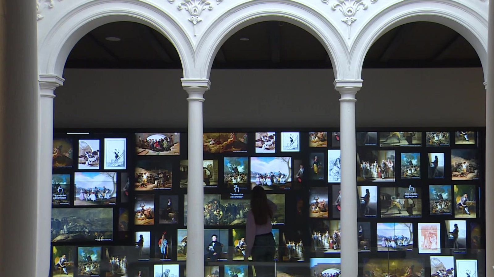 Interior del Museo Goya con arcos renacentistas y una mujer interactuando con un gran videowall digital de pantallas.