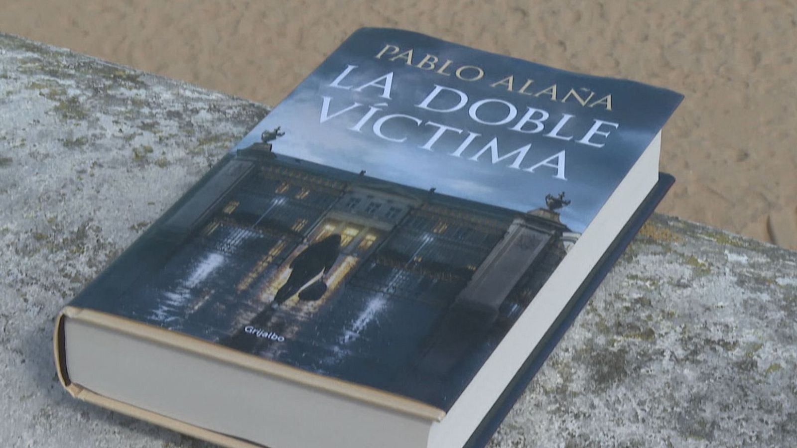 Primer plano de la novela "La doble víctima" de Pablo Alaña, apoyada sobre un muro de piedra con una portada de suspense que muestra una escena nocturna bajo la lluvia.