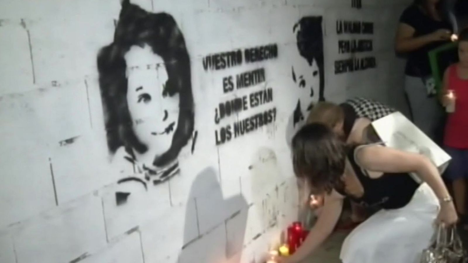 Vigilia nocturna con velas y un muro con retratos estarcidos e inscripciones reivindicativas en memoria de menores.