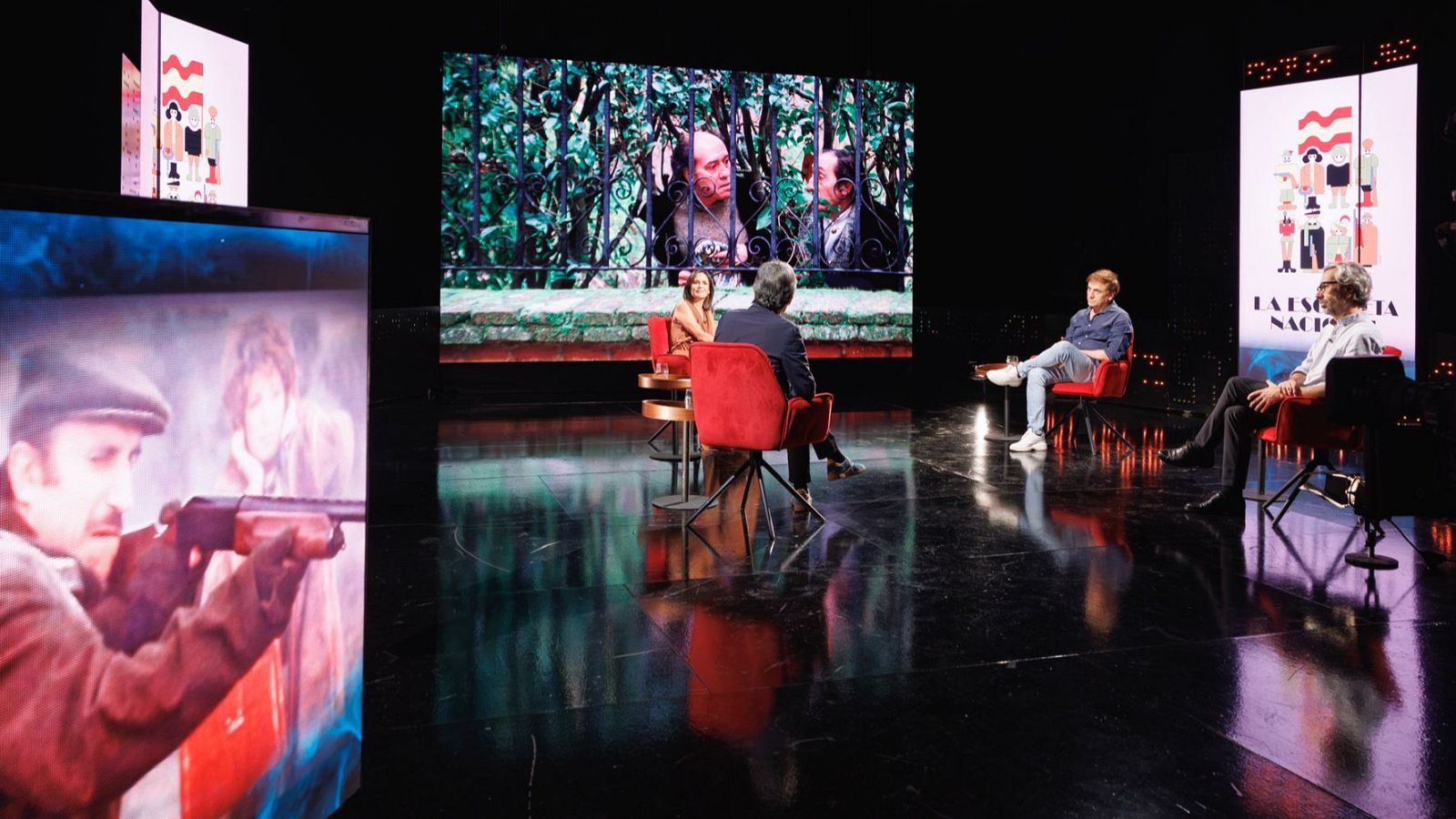 Plató de un programa de cine con cuatro personas sentadas en butacas rojas y grandes pantallas que muestran fotogramas de la película 'La escopeta nacional'.