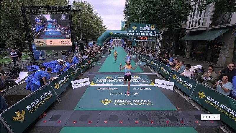 Una atleta celebra su llegada a la meta alzando los brazos en una competición de medio maratón urbana rodeada de público y arcos inflables.