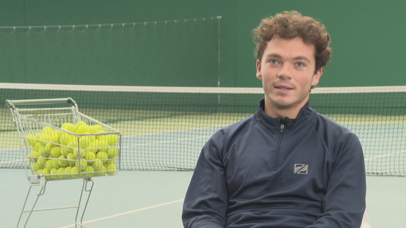 El tenista Iñaki Montes sonríe levemente mientras es entrevistado en una pista de tenis junto a un carrito de pelotas.