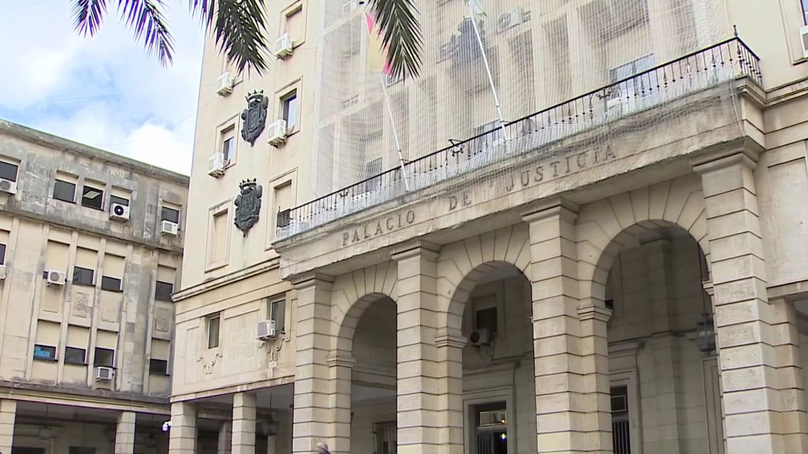 Fachada principal del Palacio de Justicia con pórtico de sillería almohadillada, arcos de medio punto y una balconada con la bandera de España bajo un cielo con nubes ligeras.