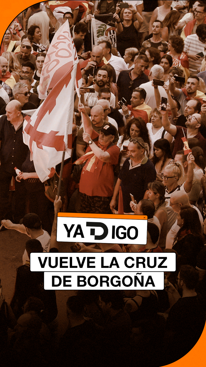 Multitud congregada en una manifestación diurna donde resalta una bandera con la Cruz de Borgoña y un rótulo inferior con el texto 'VUELVE LA CRUZ DE BORGOÑA'.