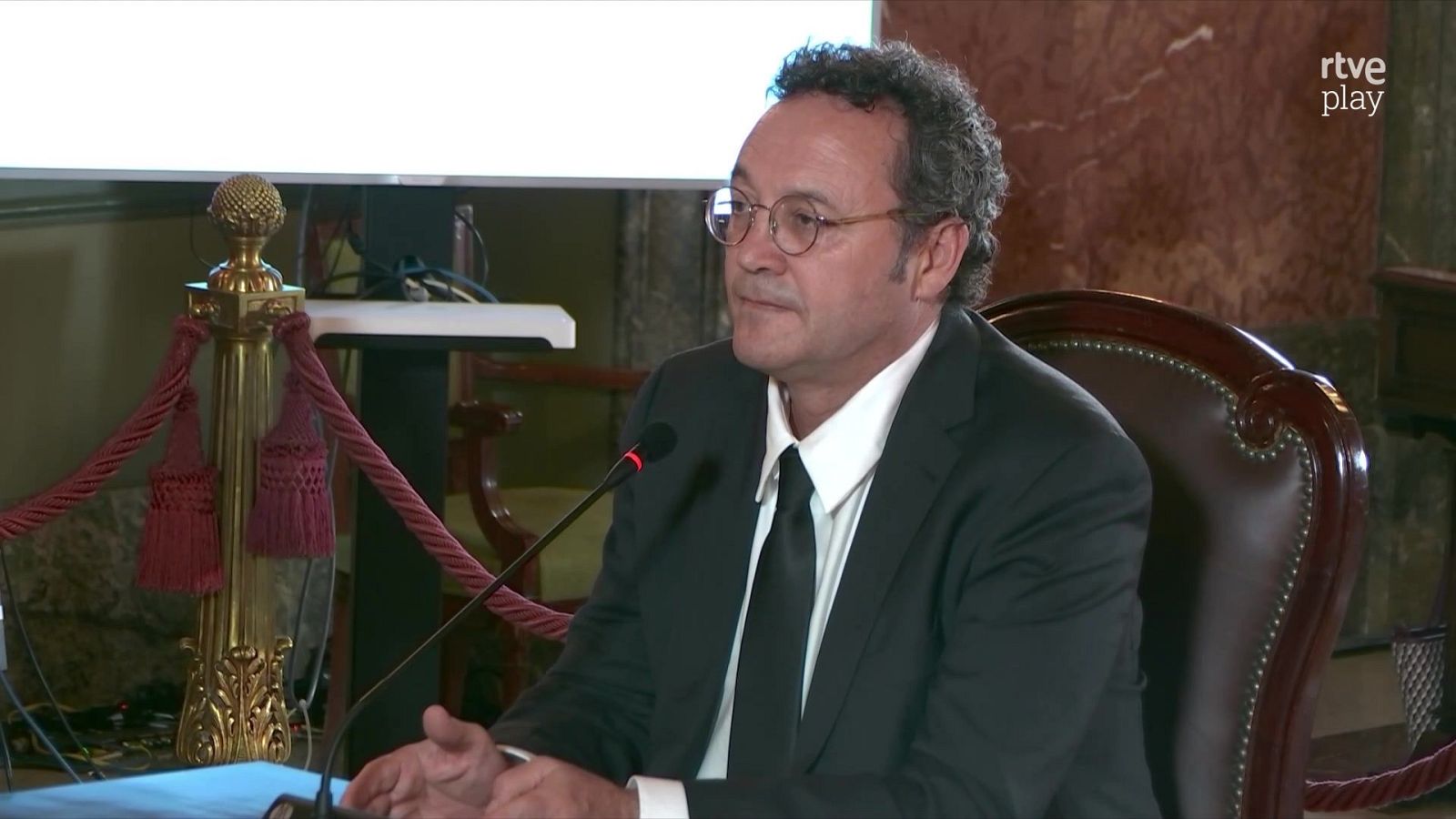 Álvaro García Ortiz en comparecencia institucional con traje oscuro, camisa blanca, corbata negra y gafas.