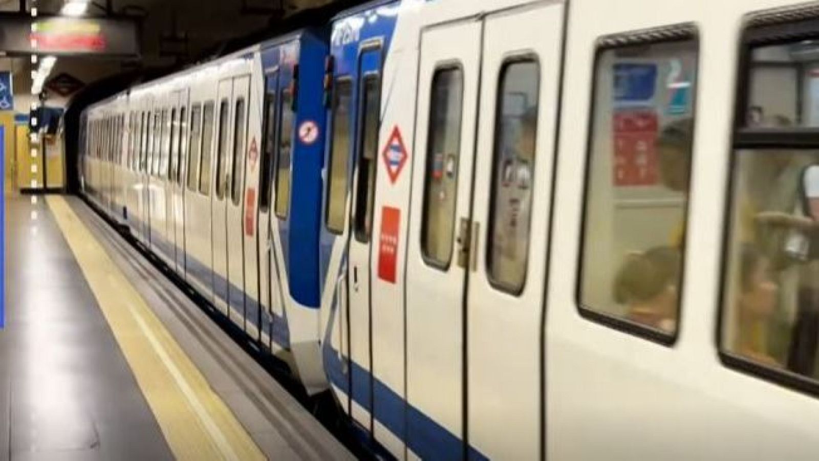 Tren de metro detenido junto al andén en una estación subterránea con el rombo tricolor corporativo.