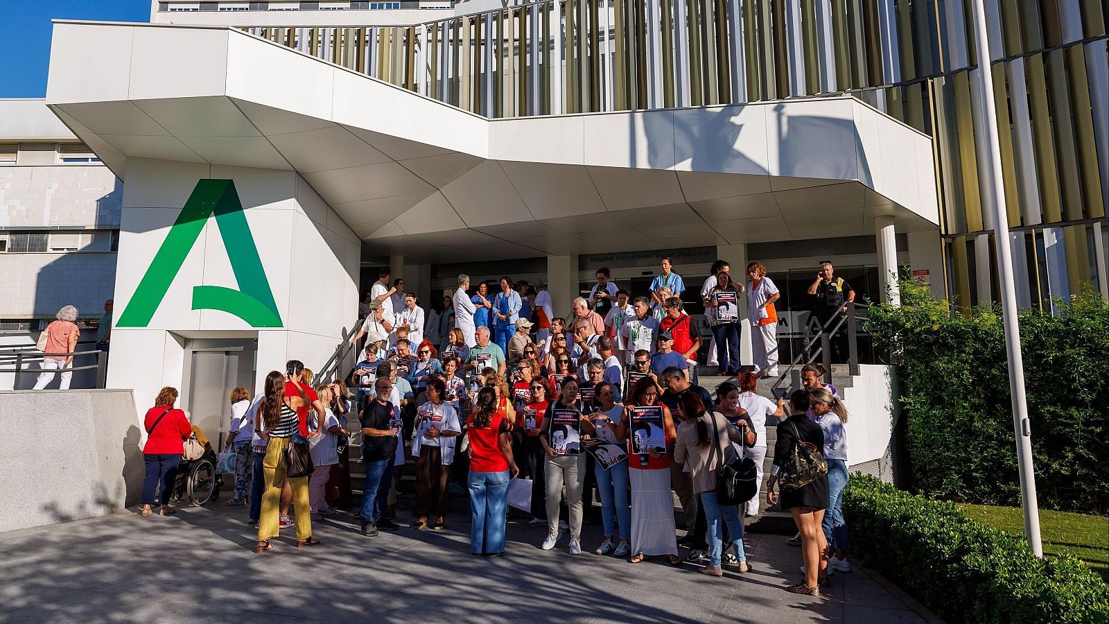 Multitud de personas y sanitarios concentrados en las escalinatas de un hospital público junto a una marquesina con el logotipo de la Junta de Andalucía.