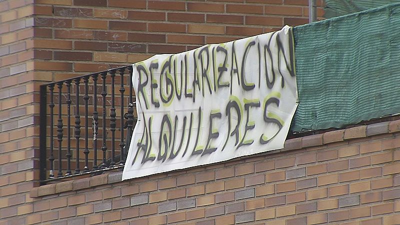 Pancarta blanca colgada en la barandilla de un balcón con el mensaje de denuncia sobre la regularización de alquileres.
