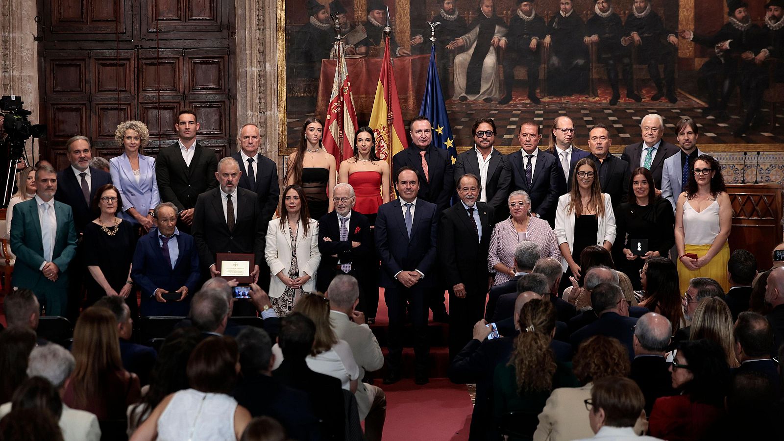 Foto de familia de la entrega de Altas Distinciones de la Generalitat con Carlos Mazón y los galardonados ante un mural histórico y banderas oficiales.