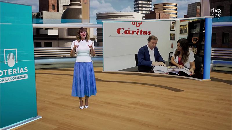 La presentadora Sandra Daviú en el plató del programa, vistiendo blusa blanca y falda azul, sonriendo ante una pantalla con imágenes de Cáritas y un fondo urbano.