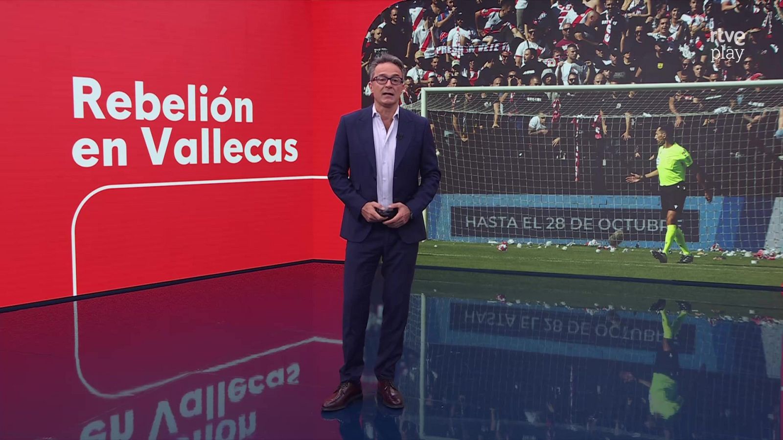 El periodista Paco Caro presenta un informativo en un plató con pantalla curva que muestra la noticia de fútbol Rebelión en Vallecas.