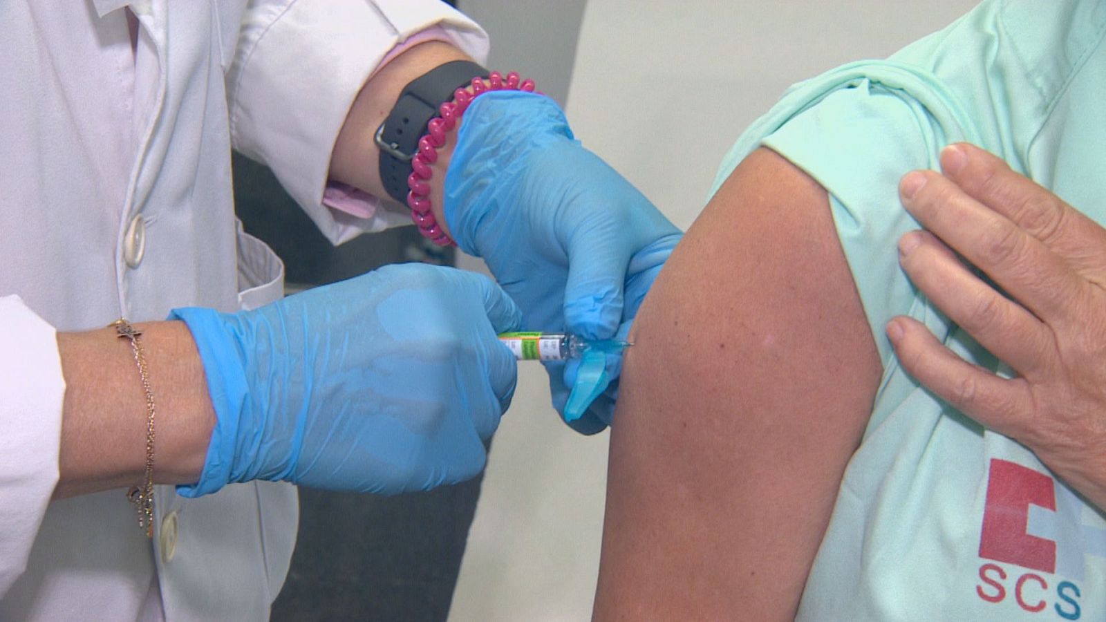 Plano detalle de un sanitario con bata blanca administrando una vacuna en el brazo de una persona que viste prenda verde con el logotipo del SCS.