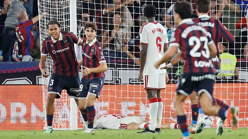 Dos futbolistas del Levante UD celebran un gol con euforia junto a la red, mientras un jugador del Alcorcón lamenta la derrota.