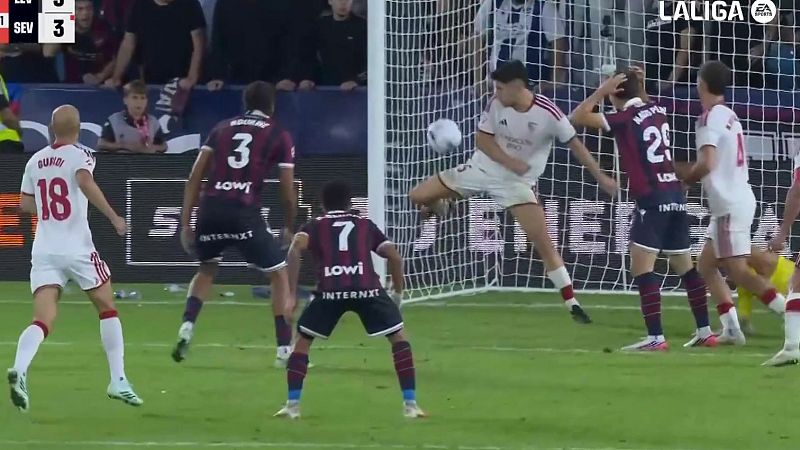 Un delantero del Sevilla FC salta para rematar el balón en el área durante un partido de fútbol, rodeado por jugadores del equipo rival.