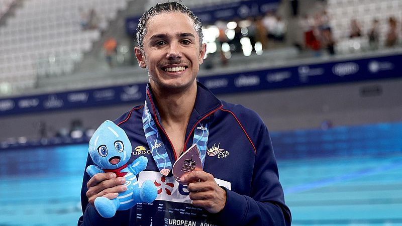 El nadador Fernando Díaz del Río posa sonriente junto a una piscina con la chaqueta de la selección española, una medalla plateada y un peluche de gota de agua.