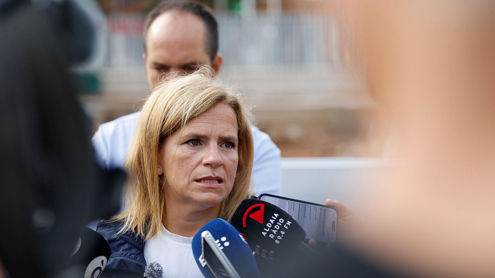 Pilar Bernabé atiende a los medios al aire libre rodeada de micrófonos, destacando uno de Aldaia Ràdio.
