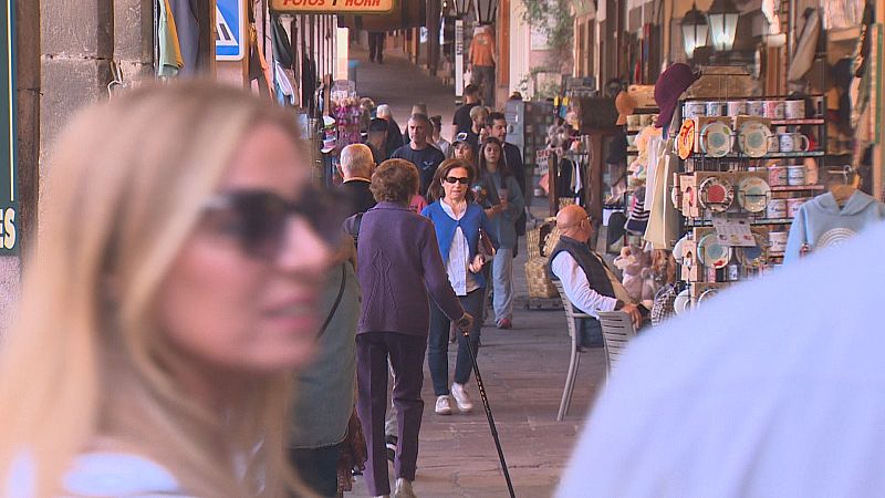 Calle peatonal soportalada y concurrida con turistas paseando, tiendas de recuerdos y personas en primer plano.