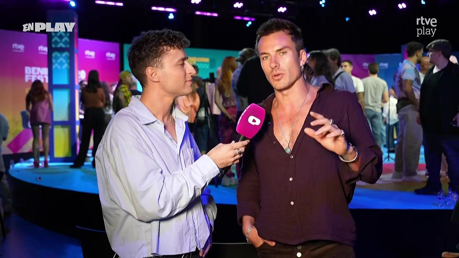 Entrevista al cantante Andrés Koi en un plató con iluminación morada y fucsia, sosteniendo el entrevistador un micrófono con logotipo de Playz.