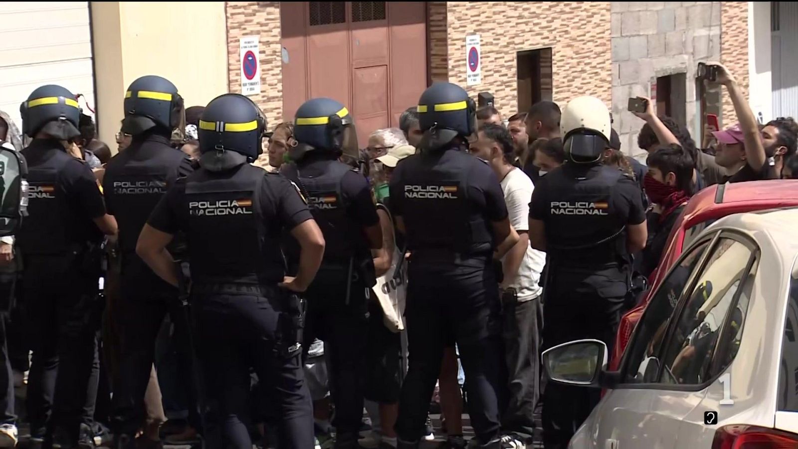 Agentes antidisturbios de la Policía Nacional de espaldas en una calle frente a una multitud durante el día.