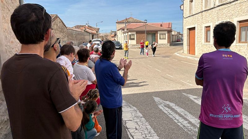 Participantes y vecinos disfrutan de la Carrera del Henar en Viloria, con corredores avanzando por una calle tradicional rodeada de casas de piedra.