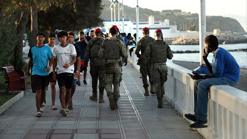 Soldados con boinas rojas patrullan el paseo marítimo de Ceuta mientras se cruzan con varios jóvenes migrantes.