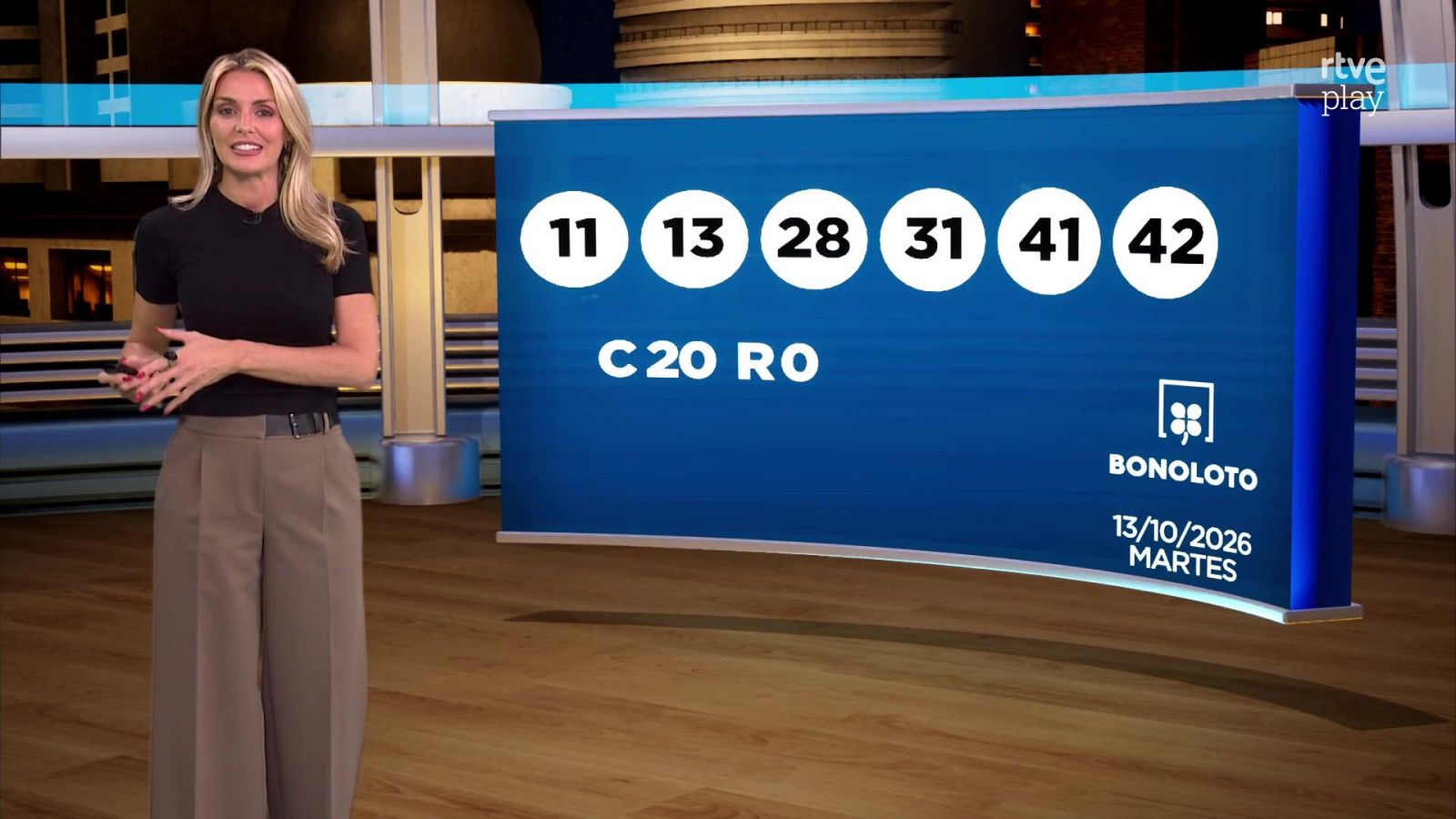 Sandra Daviú presenta los resultados de la Bonoloto en un plató de televisión, mostrando la combinación ganadora en un panel azul.