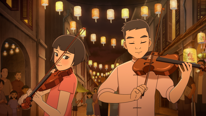 Dos jóvenes músicos tocan el violín en una calle nocturna iluminada por farolillos, acompañados por un público atento.