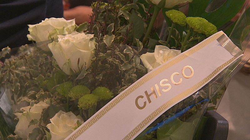 Ramo floral de homenaje con rosas blancas y una cinta blanca con el nombre 'CHISCO' impreso en letras doradas.