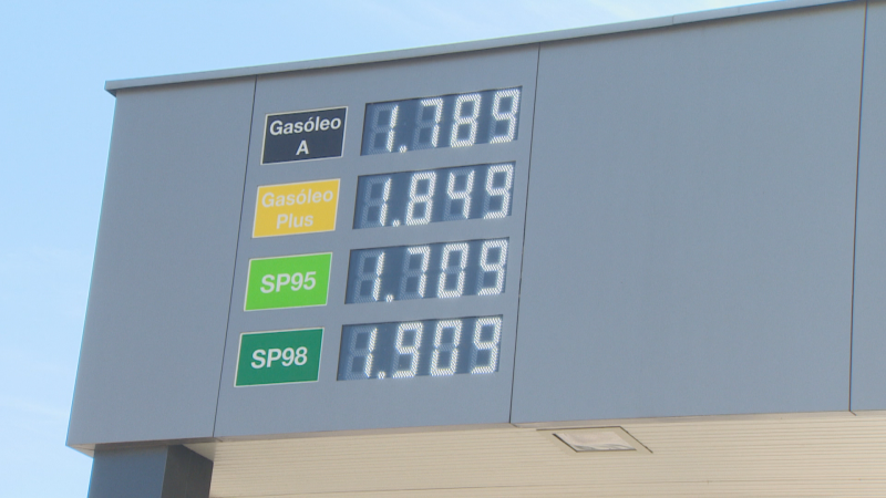 Panel digital de una gasolinera que muestra los precios por litro de cuatro tipos de carburante con números LED blancos sobre fondos de colores bajo un cielo azul.