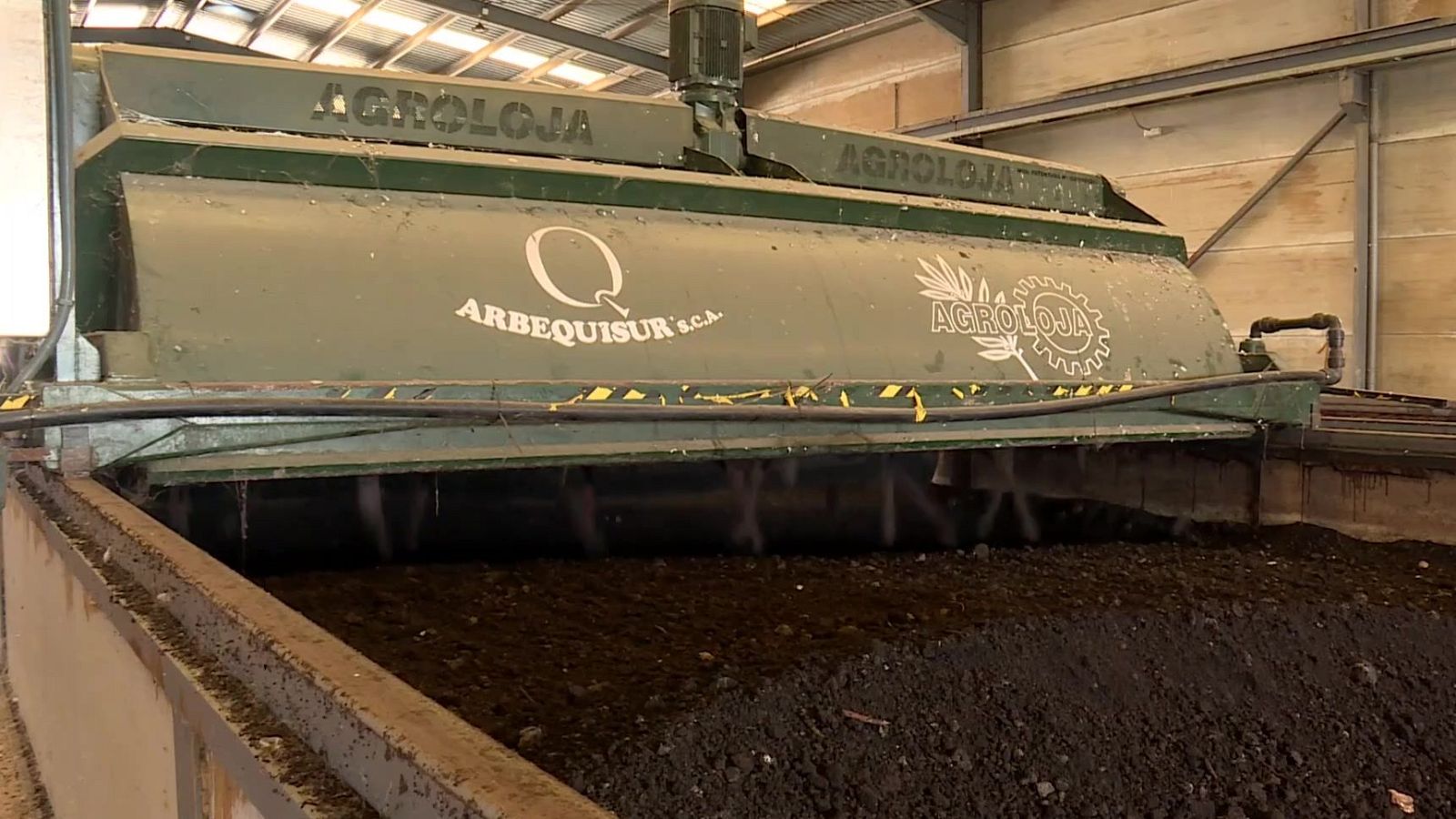 Máquina removedora verde procesando alperujo en una almazara, con los textos 'ARBEQUISUR S.C.A.' y 'AGROLOJA' visibles en su cubierta.